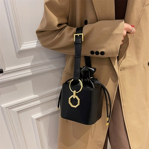 Modern black leather drawstring bucket bag with gold hardware worn over a camel coat