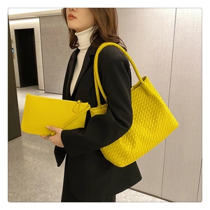Detail of bright yellow woven tote bag set with matching clutch held by a model