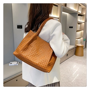 Close-up of brown woven leather tote bag featuring large plaid pattern and long handles