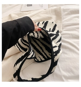 Dettaglio di una mano che tiene una borsa in maglia zebrata con texture spessa e ampia