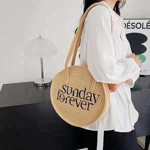 Close-up of woven straw shoulder bag featuring Sunday Forever embroidery on a model