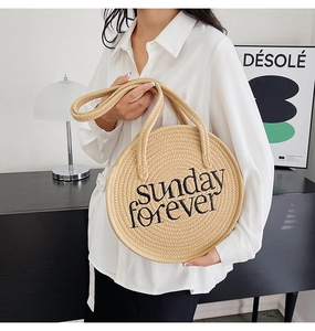 Detail of hand-woven round straw bag with Sunday Forever black embroidery and handle