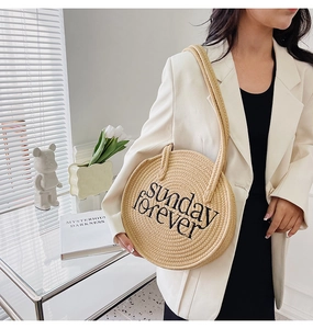 Detail of round straw shoulder bag with Sunday Forever embroidery on khaki woven texture