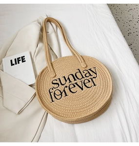 Detail of Sunday Forever embroidery on a beige woven round shoulder straw bag