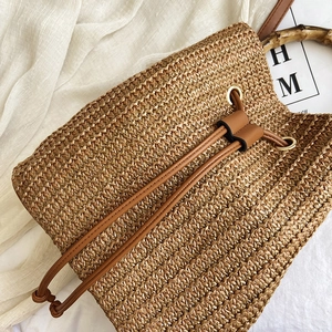 Detail of woven straw bucket bag featuring bamboo handle and brown leather drawstring