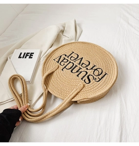Detail of round straw beach bag with Sunday Forever embroidery on a stylish white setup