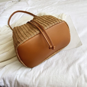 Top view of woven straw bucket bag with brown leather base and drawstring closure