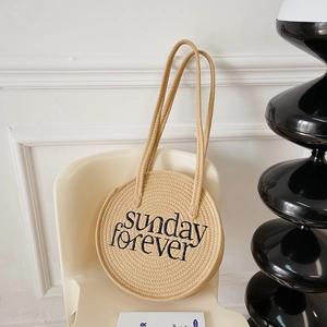 Detail of round straw bag with sunday forever embroidery on a stylish chair