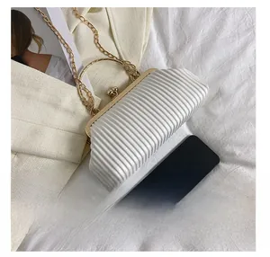 Detail of white pleated clutch bag with gold handle and chain next to a phone for size