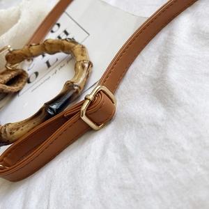Close-up of bamboo handle and brown leather strap with gold buckle on bucket bag