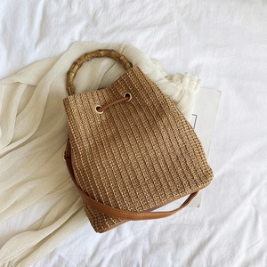 Detail of woven bucket bag featuring natural bamboo handle and brown leather drawstring