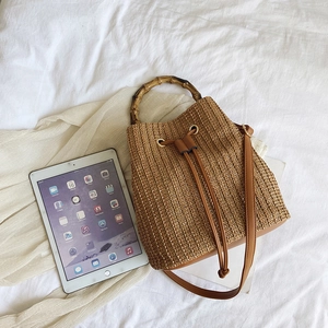 Detail of hand-woven straw bucket bag featuring bamboo handle and drawstring closure