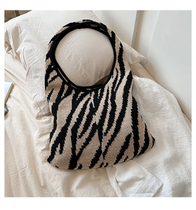 Borsa hobo in maglia con motivo zebrato giallo e nero appoggiata su biancheria da letto