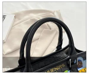 Détail du sac noir à texture crocodile avec broderie JUENIRS et anses souples