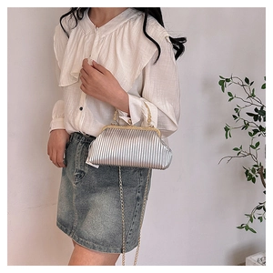 Macro detail of silver pleated clutch with vintage gold clasp and delicate chain strap