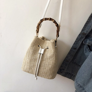 Detail of hand-woven straw bucket bag featuring bamboo handle and white leather drawstring