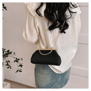 Close-up of black pleated evening bag with gold metal handle and chain strap on model