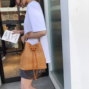 Vintage straw bucket bag with bamboo handles and crossbody strap on a model