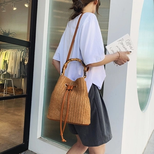 Close-up of woven straw bucket bag featuring retro bamboo handles and brown leather strap
