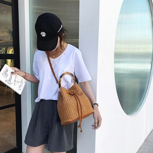 Detail of hand-woven straw bucket bag featuring natural bamboo handle and leather drawstring