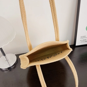 Beige straw woven tote bag with long handles in a minimalist lifestyle indoor setting
