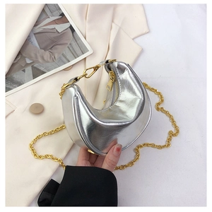 Detail of silver crescent bag with gold chain strap held against a beige blazer