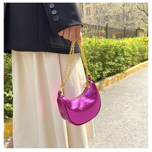 Close-up of metallic purple crescent bag with gold chain strap in outdoor setting