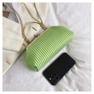 Detail of green pleated crossbody bag with gold round handle and metal chain strap