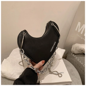 Détail d'un sac bandoulière noir en forme de cœur avec chaîne argentée et texte mode