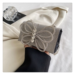 Detail of silver rhinestone bow evening clutch with metallic chain strap held by hand