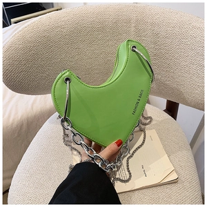 Détail du sac à main vert herbe en forme de cœur avec une grosse chaîne en argent sur chaise