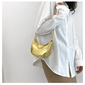 Detail of a golden crescent moon shoulder bag with metallic finish and metal chain strap