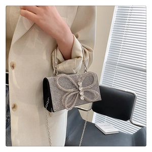 Detail of silver rhinestone evening bag featuring a large 3D crystal bow and ring handle