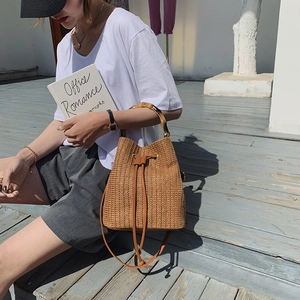 Handmade woven straw bucket bag with bamboo handle and brown leather drawstring closure