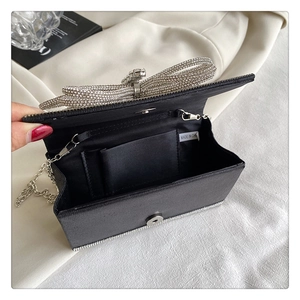 Detail of black satin evening bag featuring a silver rhinestone bow and metal chain