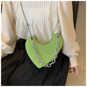 Détail du sac vert clair en forme de cœur avec chaîne argentée sur chemise blanche
