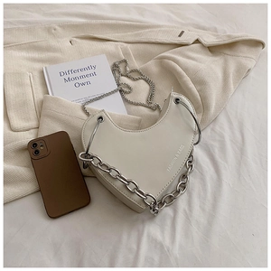 Détail d'un sac à bandoulière en forme de cœur crème avec grosse chaîne argentée et sangle