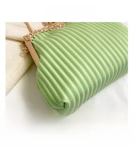 Close-up of light green pleated handbag with floral engraved gold metal clasp and PU leather