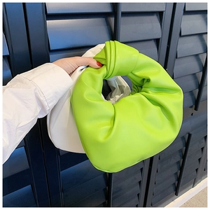 Detail view of the soft knotted handle and pleats on a bright green fashion handbag