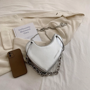 Sac à bandoulière argenté en forme de cœur pour femme sur un blazer en tweed avec livre