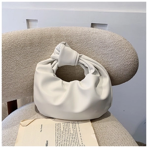 Detail of white knotted handle handbag with cloud pleats on a neutral textured surface