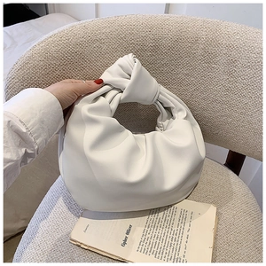 Detail of white pleated cloud bag featuring a knotted handle on a minimalist chair