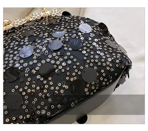 Détail de paillettes noires avec fermoir floral doré et cristaux sur un sac à bandoulière