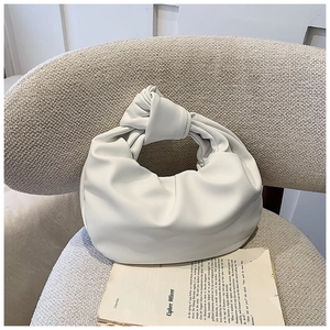 Detail of white pleated cloud bag with a knotted handle on a soft textured chair