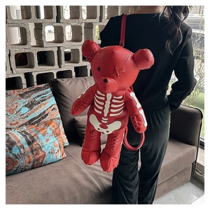 Detail view of a red leather bear backpack with skull embroidery shown on a model