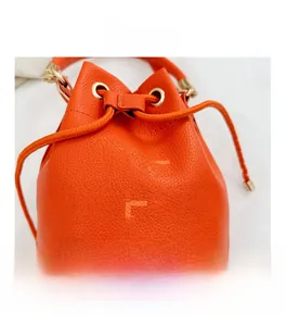 Detail of orange drawstring bucket bag featuring lychee grain leather and metal eyelets