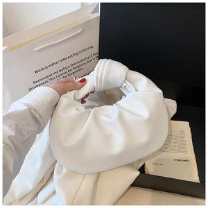 Detail of white pleated hobo bag with knotted handle in elegant gift packaging context