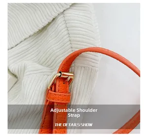 Detail of adjustable strap and gold buckle on bright orange pebbled leather bucket bag