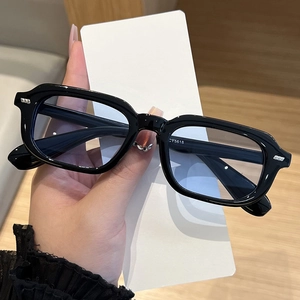 Detail of black square frame sunglasses with metal rivet accents and pale blue lenses