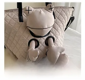 Macro detail of beige quilted tote bag featuring a padded doll with cross-eye embroidery